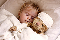 Child in bed with bandaged teddy bear