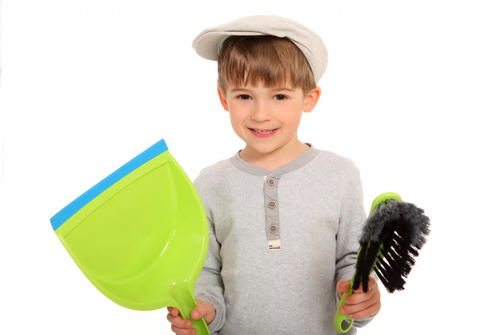 Portraitfoto eines kleinen Jungen der lächelnd mit Müllschippe und Handfeger da steht und offenbar mit saubermachen anfangen möchte...