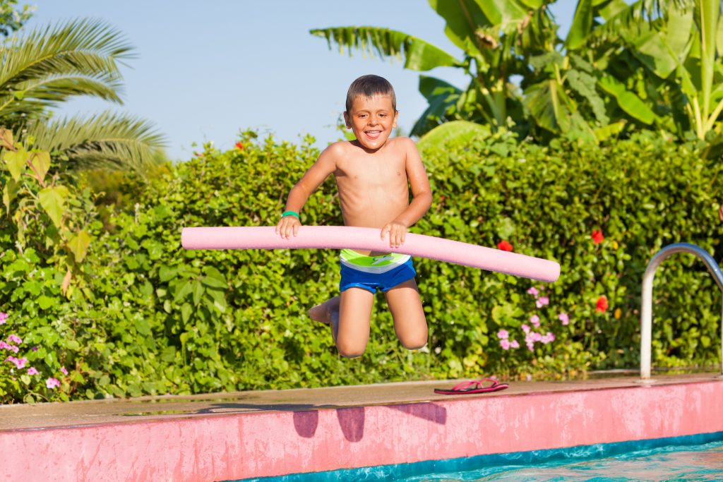 Jumping small boy holding inflatable ring standing near the swimming pool outside in summer