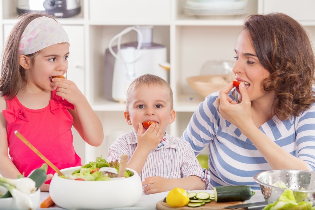 Happy young family preparing and eating vegetable salad