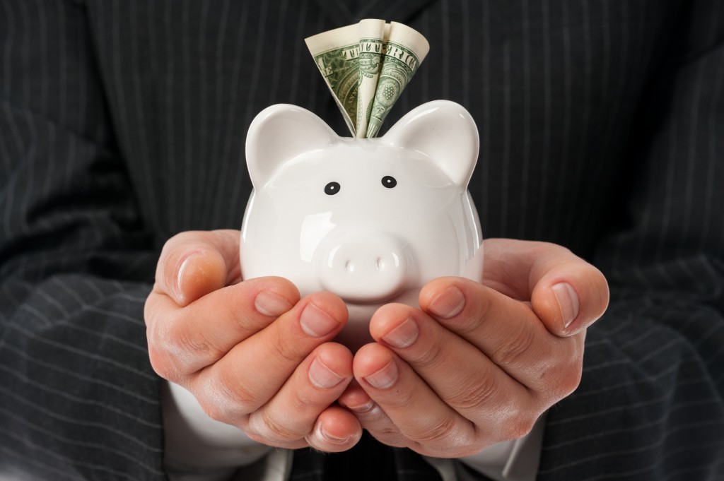 Man holding white piggy bank with dollar inside over black suit background.