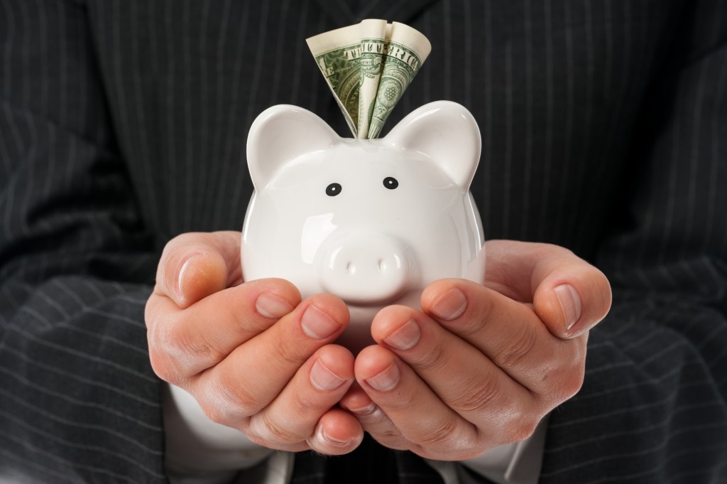 Holding piggy bank Man holding white piggy bank with dollar inside over black suit background.