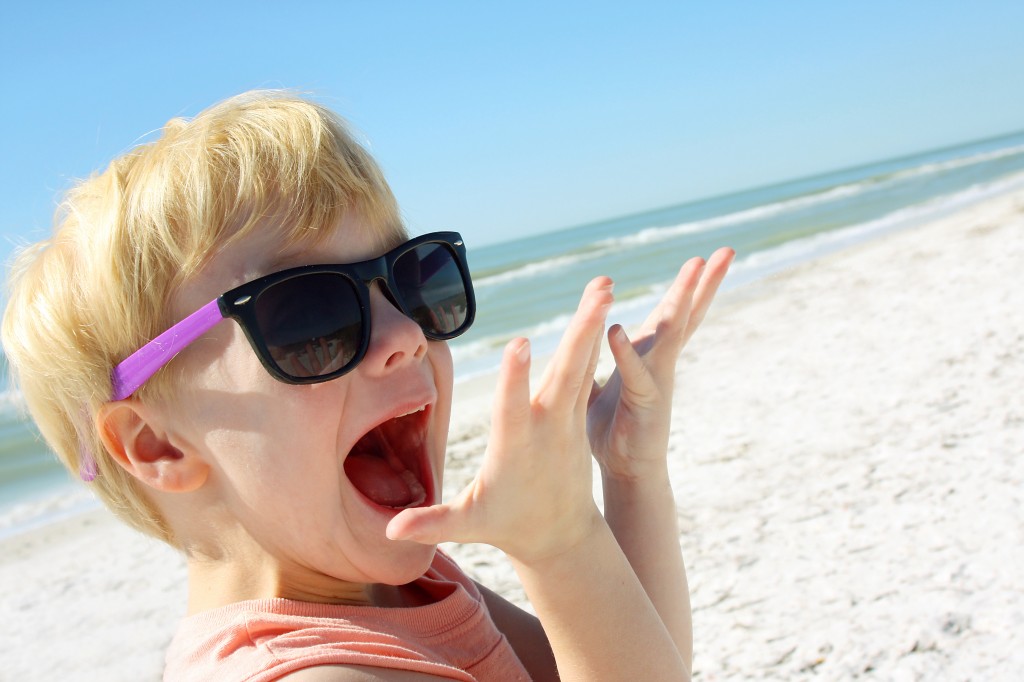 a young child is smiling and looking excited as he stands on the beach by the ocean