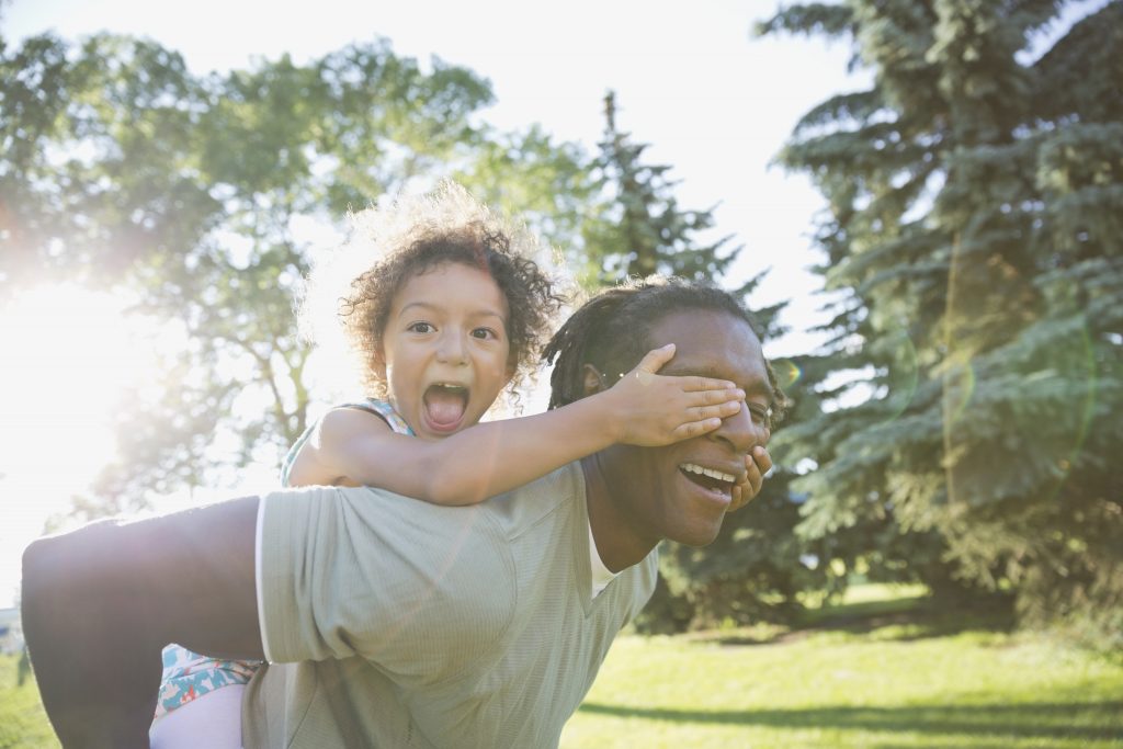 Portrait of playful girl covering fathers eyes in park