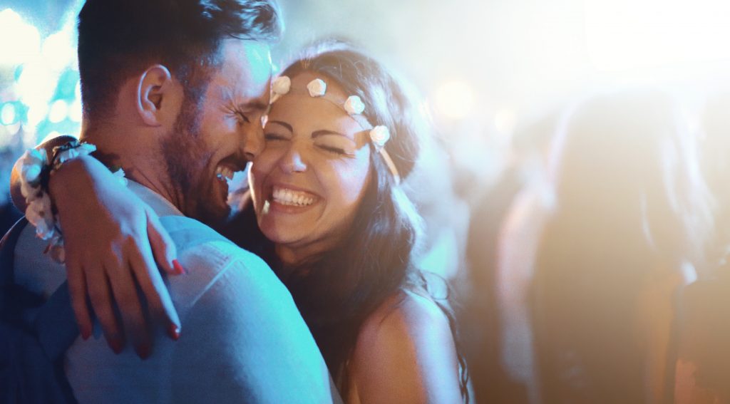 Closeup of late 20's couple on a date during an open air concert. They are having amazing time together with big crowd around them. Back lit.