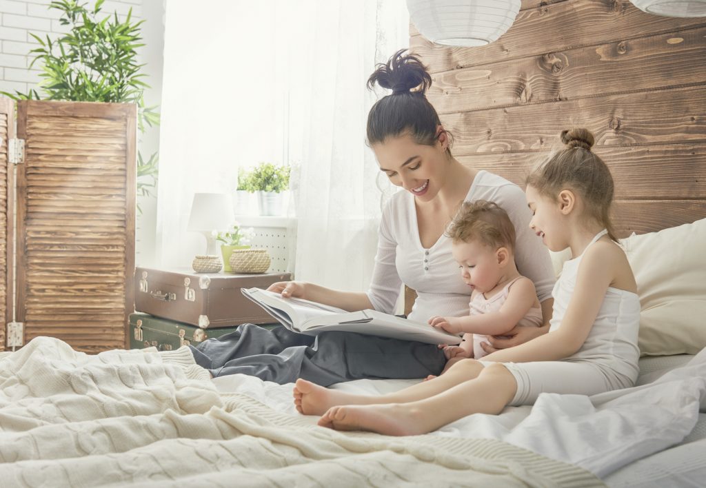 Happy loving family. Pretty young mother reading a book to her daughters.