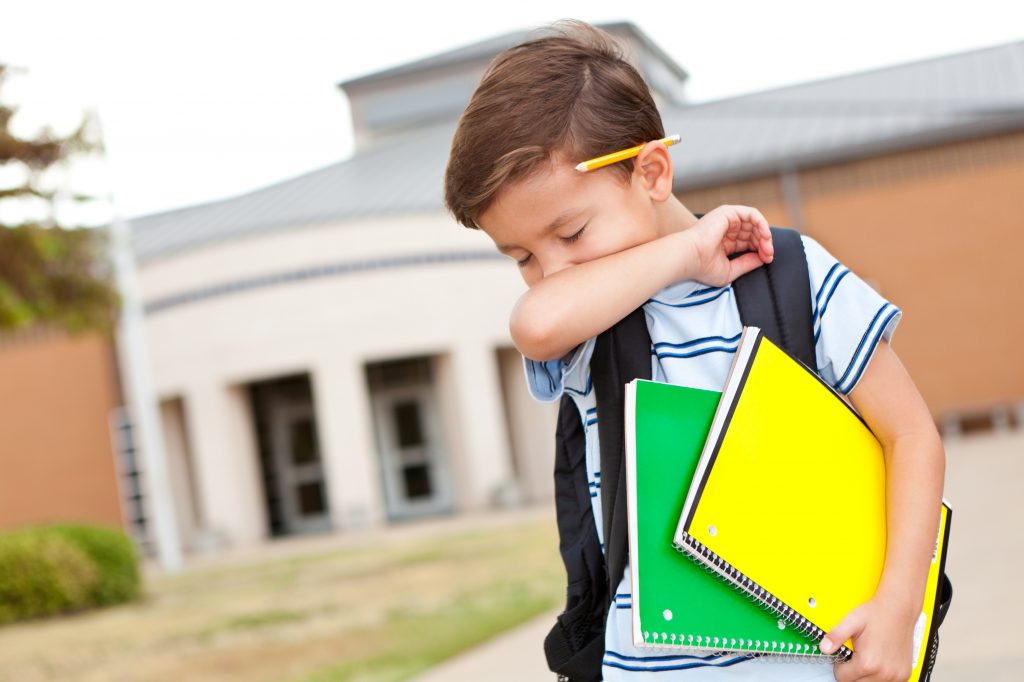 Young boy at school coughing into his arm.