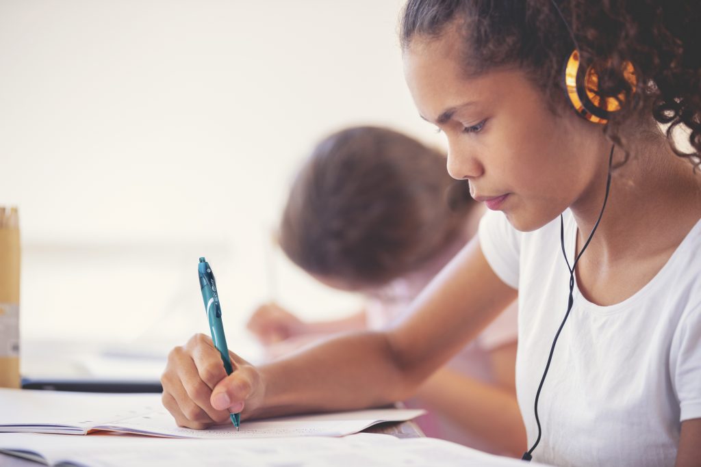 Young Aboriginal girls studying with headphones. They are working at a table at home. One girls listening to music or educational work as she works. They are sisters doing schoolwork together.