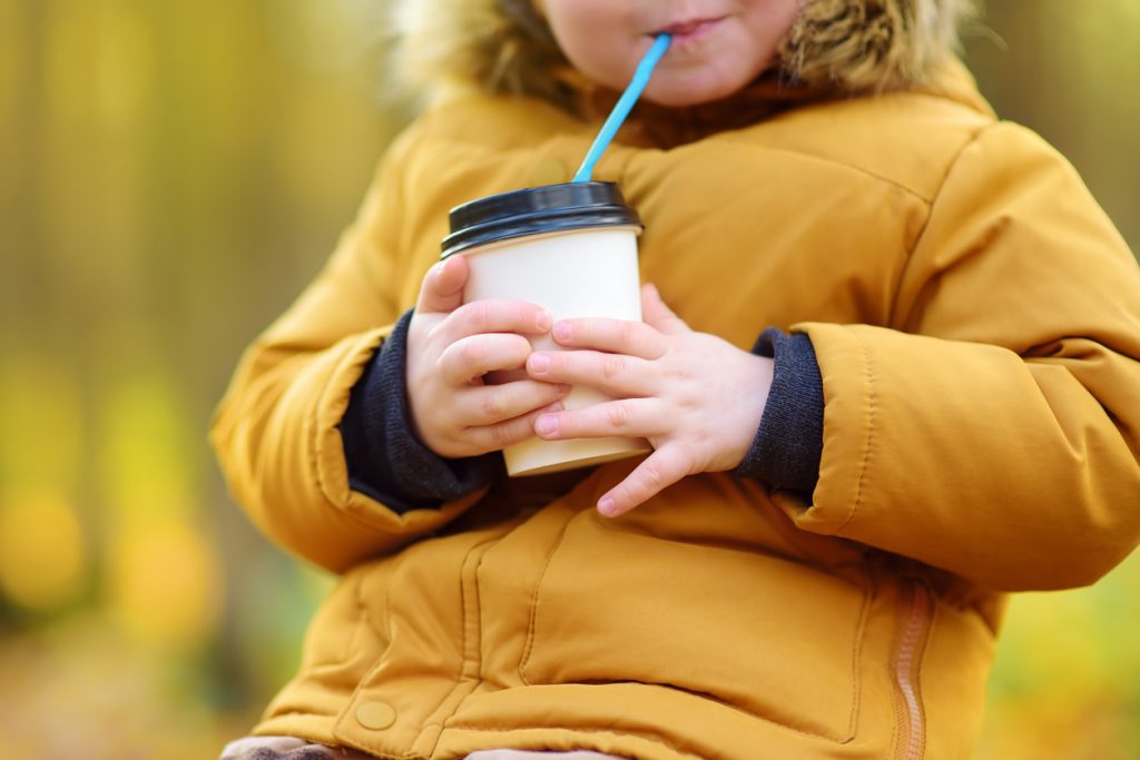 Little child walking in the forest and drinking hot cocoa at cold autumn day. Toddler boy enjoy of fall weather