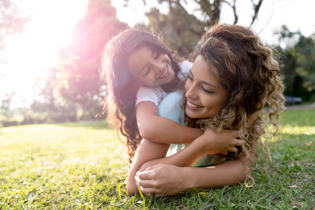 Beautiful portrait of a Latin American mother playing with her daughter outdoors and hugging - family concepts