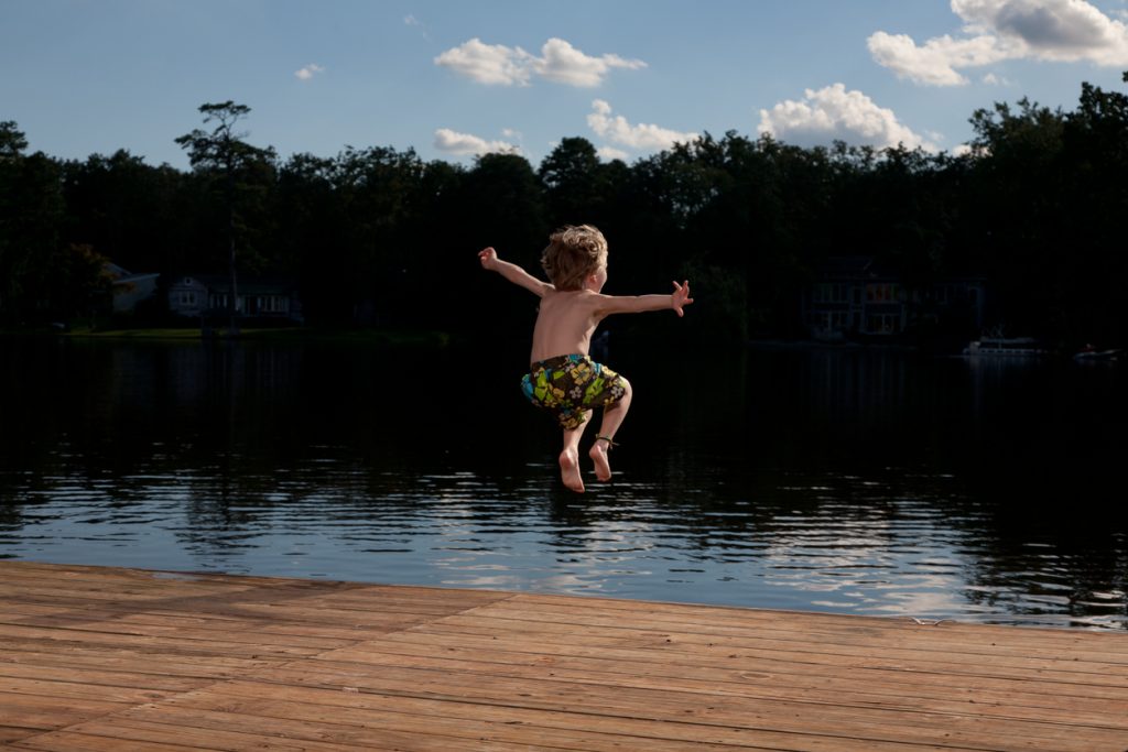 Rear view of a young boy jumping off a deck into a big lake Thank You Gifts for the Cottage - SavvyMom