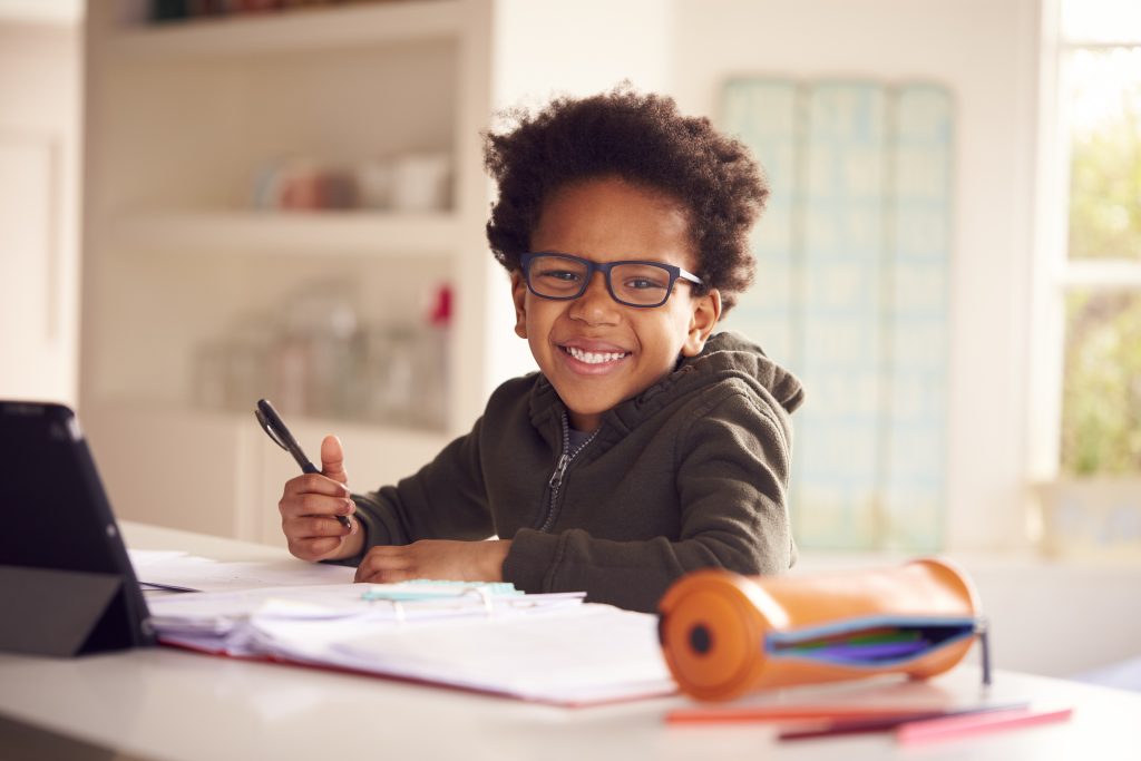 Portrait Of Boy Sitting At Kitchen Counter Doing Homework Using Digital Tablet