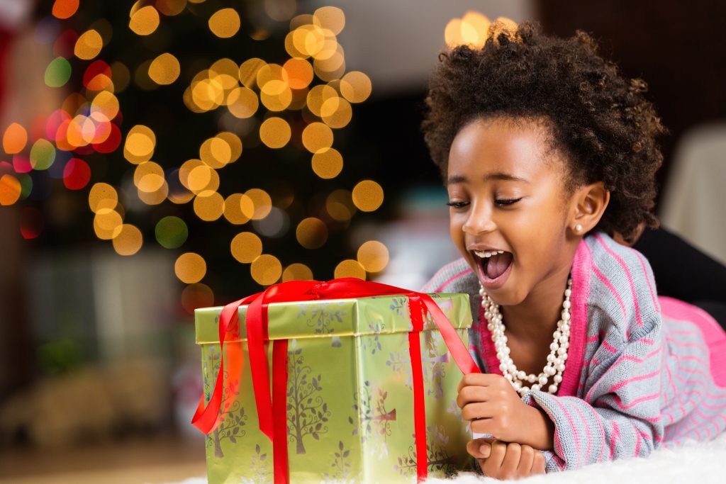 Happy little girl unwrapping Christmas present at home