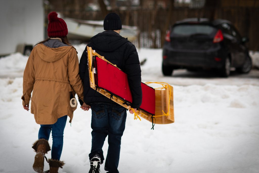 Young Couple Walk with Toboggan Budget-Friendly Winter Date Night Ideas - SavvyMom