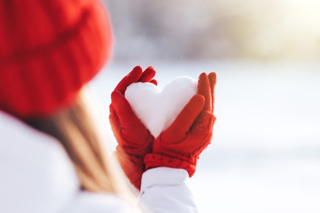 Woman in red gloves and hat holding heart shape from snow Valentine's Day in Ottawa - SavvyMom