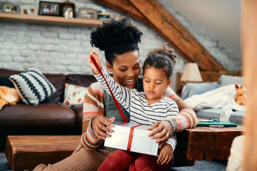 African American little girl opening a present with her mother at home.