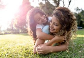 Beautiful portrait of a Latin American mother playing with her daughter outdoors and hugging - family concepts