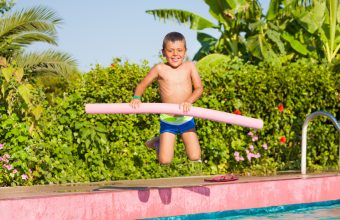 Jumping small boy holding inflatable ring standing near the swimming pool outside in summer