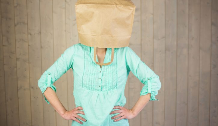 Woman covering head with brown paper bag while standing against wall
