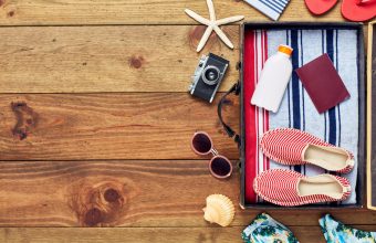Directly above shot of open suitcase with summer vacation accessories. Flat lay of travel and beach equipment. They are placed on right side of hardwood floor. The copy space on floor can be used for advertisement purpose.