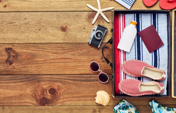 Directly above shot of open suitcase with summer vacation accessories. Flat lay of travel and beach equipment. They are placed on right side of hardwood floor. The copy space on floor can be used for advertisement purpose.