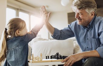 Little girl high fiving grandfather while playing chess