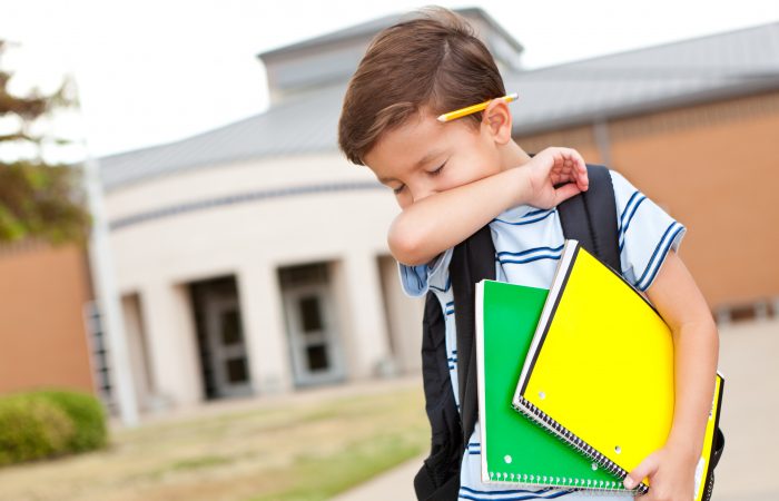 Young boy at school coughing into his arm.