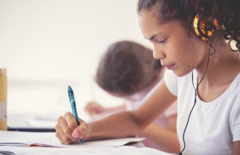 Young Aboriginal girls studying with headphones. They are working at a table at home. One girls listening to music or educational work as she works. They are sisters doing schoolwork together.