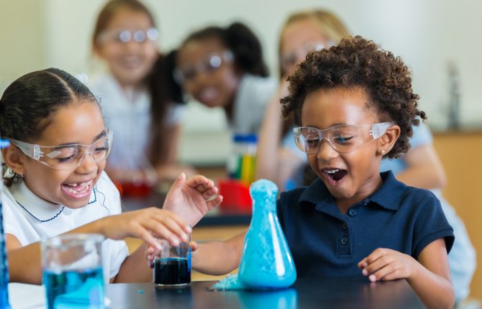 Diverse private school classmates are excited as foam overflows from beaker during chemistry experiment.