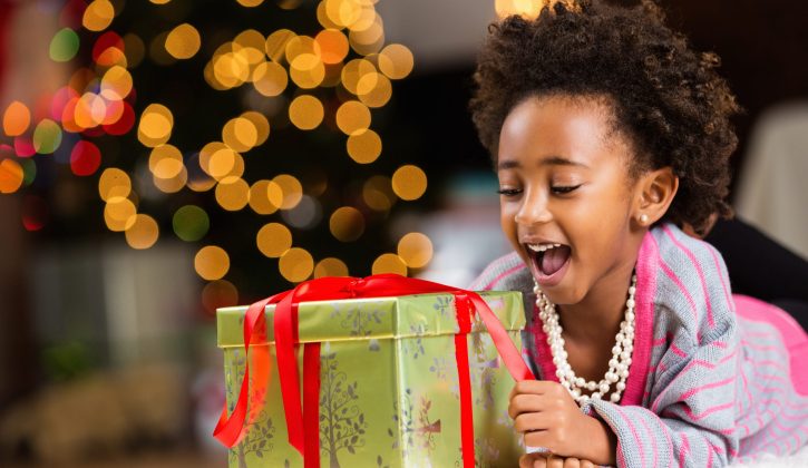 Happy little girl unwrapping Christmas present at home