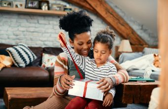 African American little girl opening a present with her mother at home.