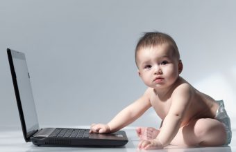Six month old baby sitting in front of a laptop computer