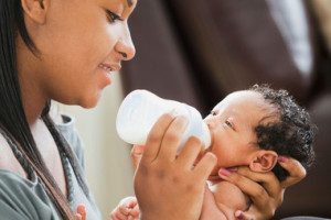 Mixed race mother feeding bottle to newborn baby